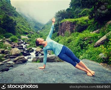 Yoga outdoors - beautiful sporty fit woman doing yoga asana Vasisthasana - side plank pose at tropical waterfall. Vintage retro effect filtered hipster style image.. Woman doing yoga asana Vasisthasana - side plank pose outdoors