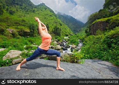 Yoga outdoors - sporty fit woman doing Ashtanga Vinyasa Yoga asana Virabhadrasana 1 Warrior pose posture at waterfall in HImalayas mountains. Woman doing Ashtanga Vinyasa Yoga asana Virabhadrasana 1 Warrior