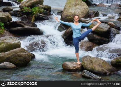 Yoga outdoors - woman doing Ashtanga Vinyasa Yoga balance asana Utthita Hasta Padangushthasana - Extended Hand-To-Big-Toe Pose position posture outdoors at waterfall. Woman doing Ashtanga Vinyasa Yoga asana outdoors at waterfall