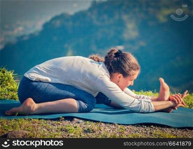Yoga outdoors - woman doing Ashtanga Vinyasa yoga Tiryam-Mukha Eka-Pada Paschimottanasana asana stretching position outdoors. Vintage retro effect filtered hipster style image.. Woman in Tiryam-Mukha Eka-Pada Paschimottanasana asana stretchin