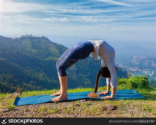 Yoga outdoors - young sporty fit woman doing Ashtanga Vinyasa Yoga asana Urdhva Dhanurasana  - upward bow pose - in Himalayas mountains in the morning  Himachal Pradesh, India. Woman doing Ashtanga Vinyasa Yoga asana Urdhva Dhanurasana outdoors