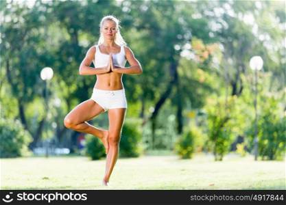 Yoga practice. Young woman in white in summer park practicing yoga