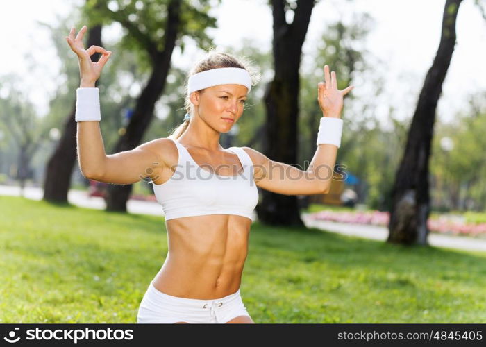 Yoga practice. Young woman in white sitting on grass and practicing yoga