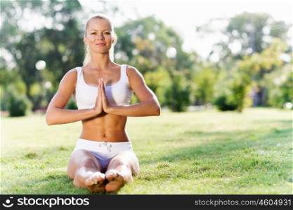 Yoga practice. Young woman in white sitting on grass in lotus pose