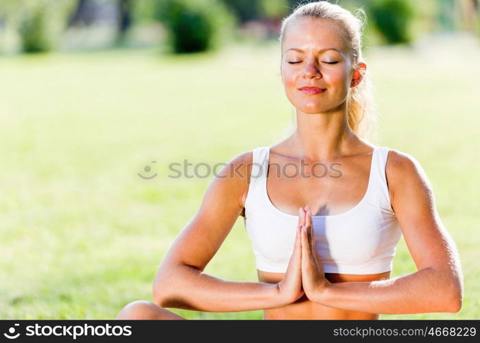 Yoga practice. Young woman in white sitting on grass in lotus pose