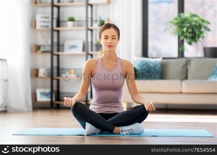 yoga, sport and healthy lifestyle concept - woman meditating in lotus pose at home. woman doing yoga in lotus pose at home
