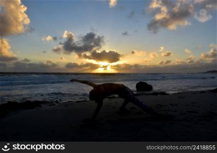 Yoga wild thing pose silhouetted at sunrise along the coastline.