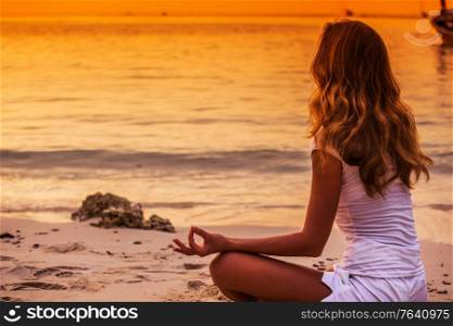 Yoga woman in lotus pose on sea coast at sunset. Sunset yoga woman