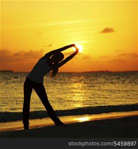 Yoga woman in serene sunset at beach doing stretching workout