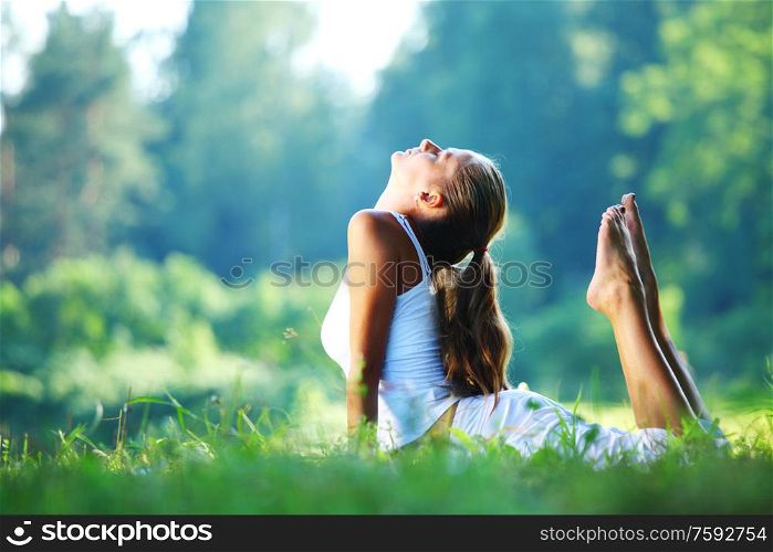 Yoga woman in white on green park grass in cobra asana pose. Yoga woman in park
