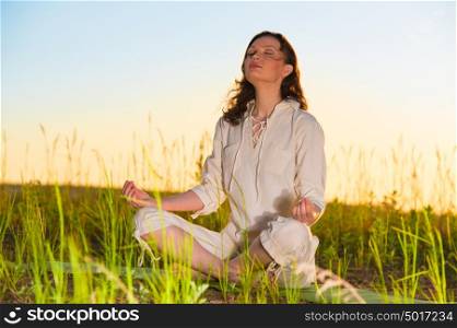 Yoga woman meditating on green grass against the sun
