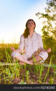 Yoga woman meditating on green grass against the sun