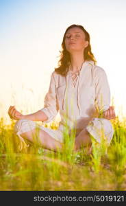 Yoga woman meditating on green grass against the sun