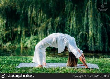 Yoga woman practicing outdoors, doing a bridge pose, green natural background. Yoga Woman Doing Bridge Pose, Natural Green Background