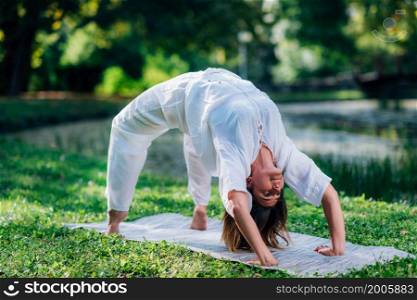 Yoga woman practicing outdoors, doing a bridge pose, green natural background. Yoga Woman Doing Bridge Pose, Natural Green Background