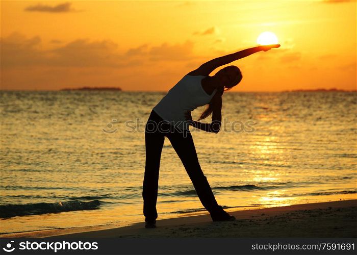Yoga woman silhouette over sunset sky and sea background. Sunset yoga woman