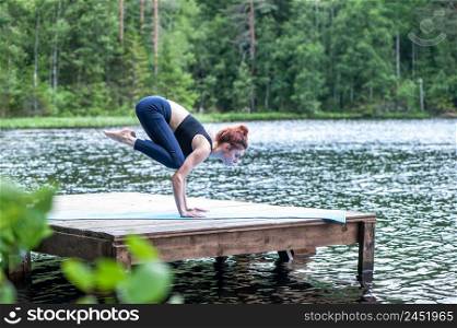Yogi girl practicing yoga, doing Bakasana exercise, Crane pose, on the lake. Concept of healthy life and natural balance