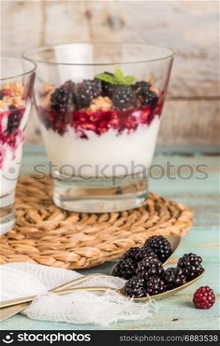 Yogurt desert with raspberries, blackberry and mint. Focus on spoons with blackberries.