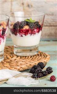 Yogurt desert with raspberries, blackberry and mint. Focus on spoons with blackberries.