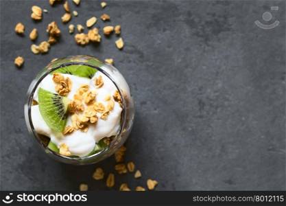 Yogurt parfait with fresh kiwi and crunchy almond and oatmeal granola in glass, photographed overhead on slate with natural light (Selective Focus, Focus on the top of the parfait)