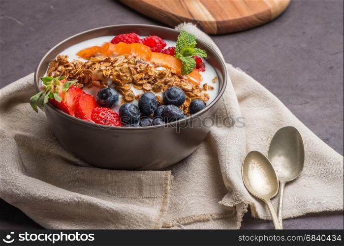 Yogurt with baked granola and berries in small bowl strawberries blueberries. Granola baked with nuts and honey for little sweetness.