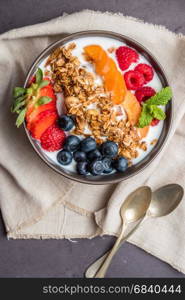 Yogurt with baked granola and berries in small bowl strawberries blueberries. Granola baked with nuts and honey for little sweetness.