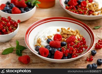 Yogurt with berries on wooden background. White plain greek yogurt with fresh berries and granola, top view. Healthy food, breakfast menu