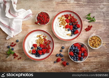 Yogurt with berries on wooden background. White plain greek yogurt with fresh berries and granola, top view. Healthy food, breakfast menu