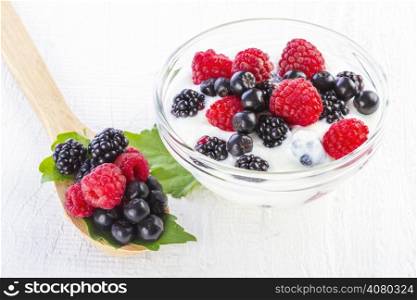 yogurt with forest berries in bowl on white wooden background