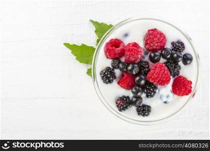 yogurt with forest berries in bowl on white wooden table