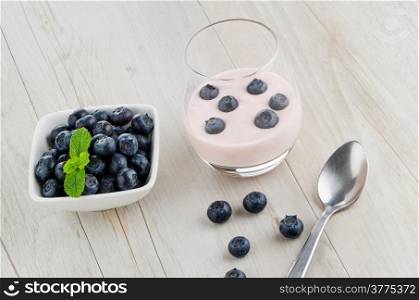 Yogurt with fresh blueberries on a wooden table set.