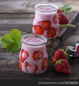 yogurt with fresh red strawberries in a glass jar on a gray wooden table, close up. yogurt with fresh red strawberries in a glass jar