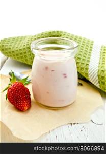 Yogurt with strawberries in a glass jar, strawberry and mint on parchment, towel on a background of wooden board