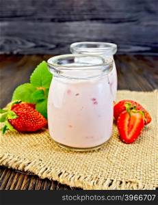 Yogurt with strawberries in two glass jar on a napkin of burlap with berries and mint on a wooden boards background