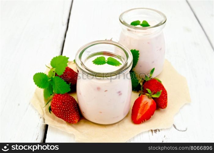 Yogurt with strawberries in two glass jars, strawberry and mint on a parchment background on wooden board