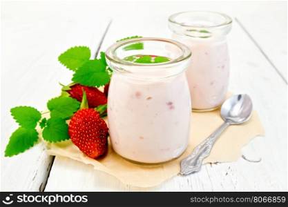 Yogurt with strawberries in two jars and a spoon, strawberries and mint on parchment on the background light wooden boards