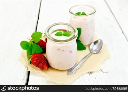 Yogurt with strawberries in two jars and a spoon, strawberries and mint on a parchment background on wooden board
