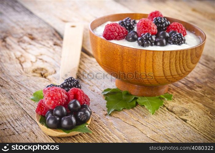 yogurt with wild berries in wooden bowl on wooden background