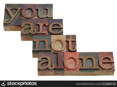 you are not alone - words in vintage wooden letterpress printing blocks, stained by color inks, isolated on white