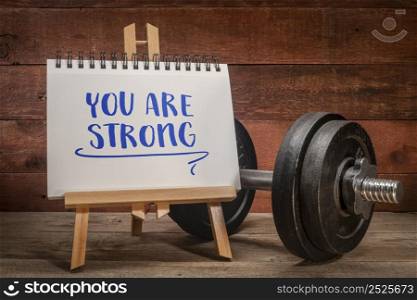 you are strong positive affirmation, a small easel sign with a heavy dumbbell, fitness and personal development concept
