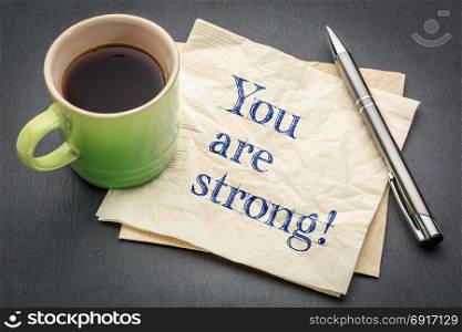 You are strong positive affirmation - handwriting on a napkin with cup of coffee against gray slate stone background