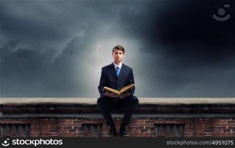 You knowledge is your future!. Handsome businessman sitting on top and reading book