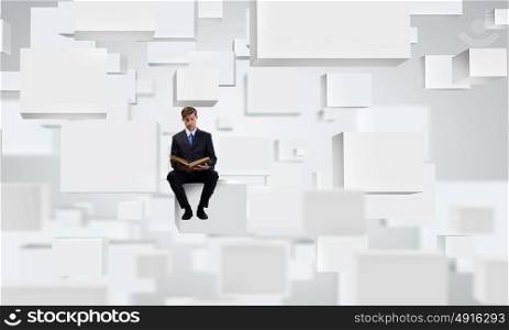 You knowledge is your future!. Handsome businessman sitting on white cube and reading book