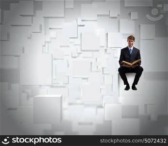 You knowledge is your future!. Handsome businessman sitting on white cube and reading book