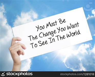 You Must Be The Change You Want To See In The World Sign on white paper. Man Hand Holding Paper with text. Isolated on sky background. Business concept. Stock Photo