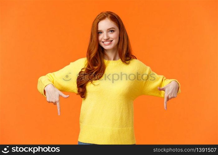 You need see this, check it out. Cheerful gorgeous redhead girl in yellow sweater, smiling and pointing down, recommend product, advertising shopping holidays sales, orange background.. You need see this, check it out. Cheerful gorgeous redhead girl in yellow sweater, smiling and pointing down, recommend product, advertising shopping holidays sales, orange background