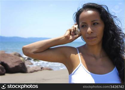 Youg latina woman listening to the sound of a shell.