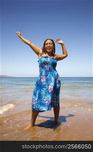Yound-adult African American woman standing in shore with arms stretched.
