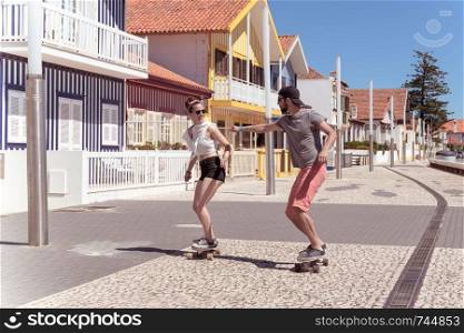 Young active couple enjoying a summer sunny day skateboarding near typical Costa Nova houses in Aveiro - Portugal.