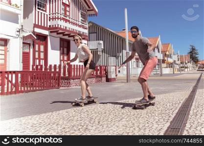 Young active couple enjoying a summer sunny day skateboarding near typical Costa Nova houses in Aveiro - Portugal.